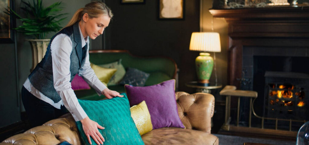 Housekeeper tidying a room with bright cushions on a sofa